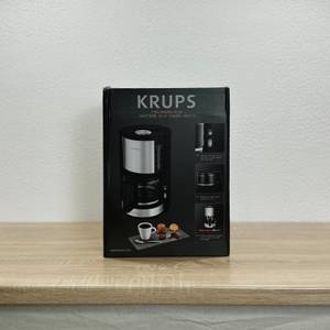 Die Frontseite der Verpackung der Krups KM3210 zeigt das Produktbild, Markenlogo und technische Merkmale der Filterkaffeemaschine.