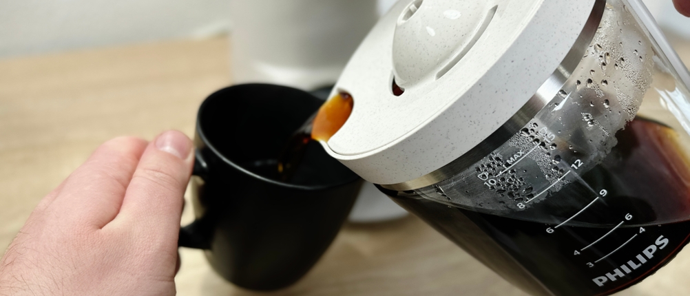 Kaffee wird aus der Glaskanne der Philips HD5120 in eine schwarze Tasse gegossen. Dampf steigt leicht auf.