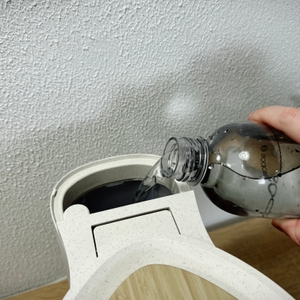 Wasser wird aus einer Flasche in den Wassertank der Philips-HD5120-Filterkaffeemaschine gegossen. Der Deckel ist geöffnet.