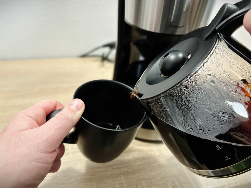 Kaffee wird aus der WMF-Bueno-Glaskanne in eine schwarze Tasse gegossen. Der Kaffee läuft direkt und mit leichtem Tropfen.