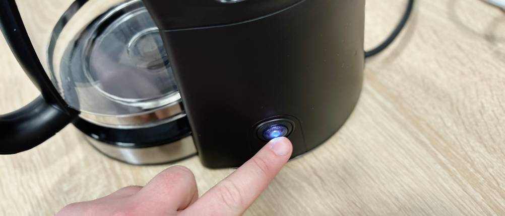 Ein Finger drückt den beleuchteten Einschaltknopf der WMF Bueno. Das Gerät ist angeschlossen und einsatzbereit.