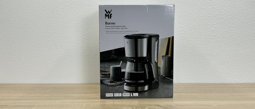 Die Verpackung der WMF-Bueno-Filterkaffeemaschine zeigt ein Produktbild und technische Angaben auf der Vorderseite. Das Design ist in Schwarz und Weiß gehalten.