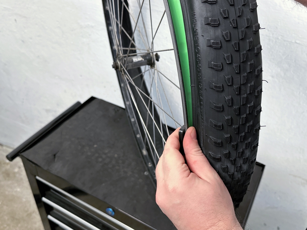 Ein Fincci-Gravel-Fahrradreifen 29 Zoll ist auf einem Laufrad montiert. Die Position der Wulst wird von Hand geprüft.