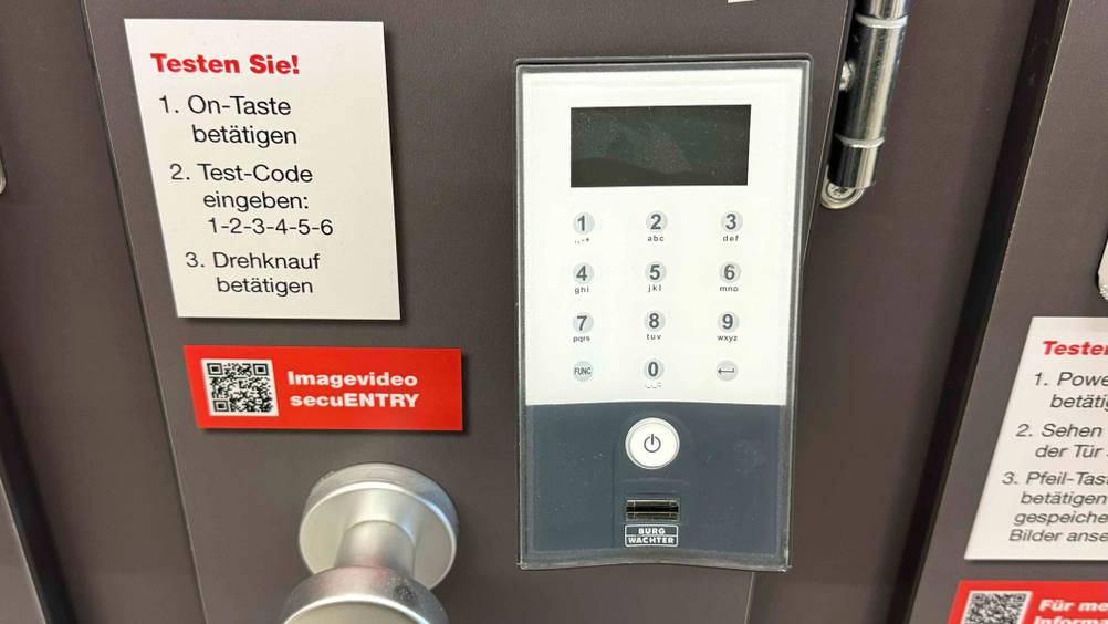 Ein Fingerprint-Türöffner im Test von vorne auf eine Ausstellungswand mit Informationen montiert.