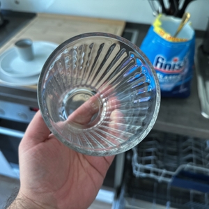 Ein sauberes Glas wird hochgehalten, im Hintergrund ist das geöffnete Finish-Spülmaschinenpulver zu sehen.