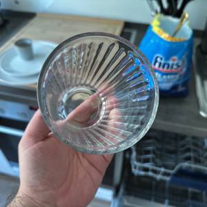 Ein sauberes Glas wird hochgehalten, im Hintergrund ist das geöffnete Finish-Spülmaschinenpulver zu sehen.