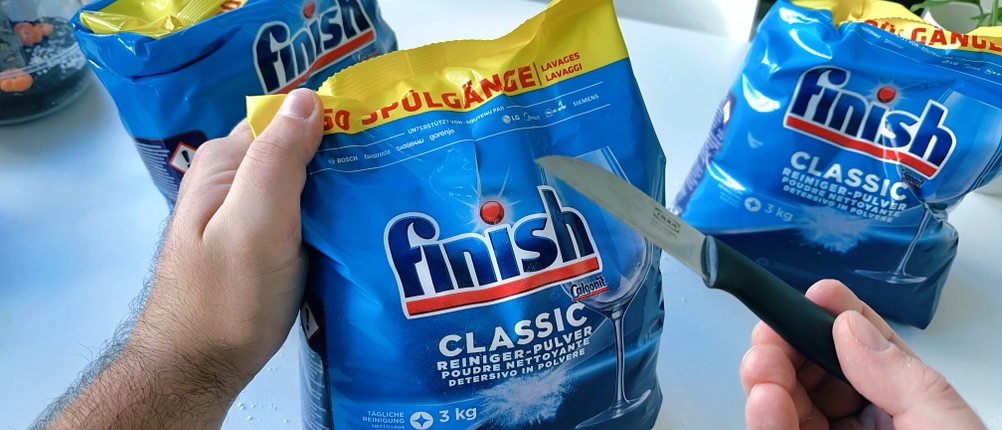 Ein Messer wird vor die Verpackung des Finish-Spülmaschinenpulvers gehalten.