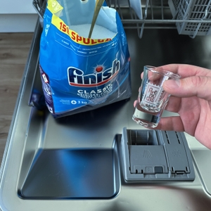 Ein Shotglas wird vor der Verpackung des Spülmaschinenpulvers von Finish hochgehoben.