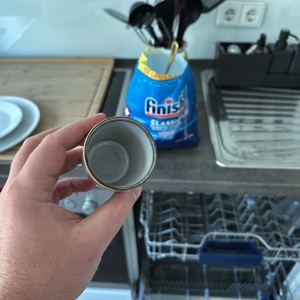 Eine gereinigte Kaffeetasse wird vor einer geöffneten Spülmaschine hochgehalten.