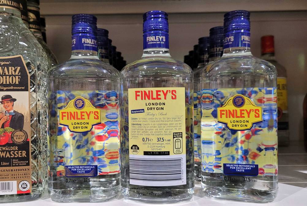 In einem Regal stehen mehrere Flaschen des getesteten Gins die mittlerer zeigt die Rückseite.