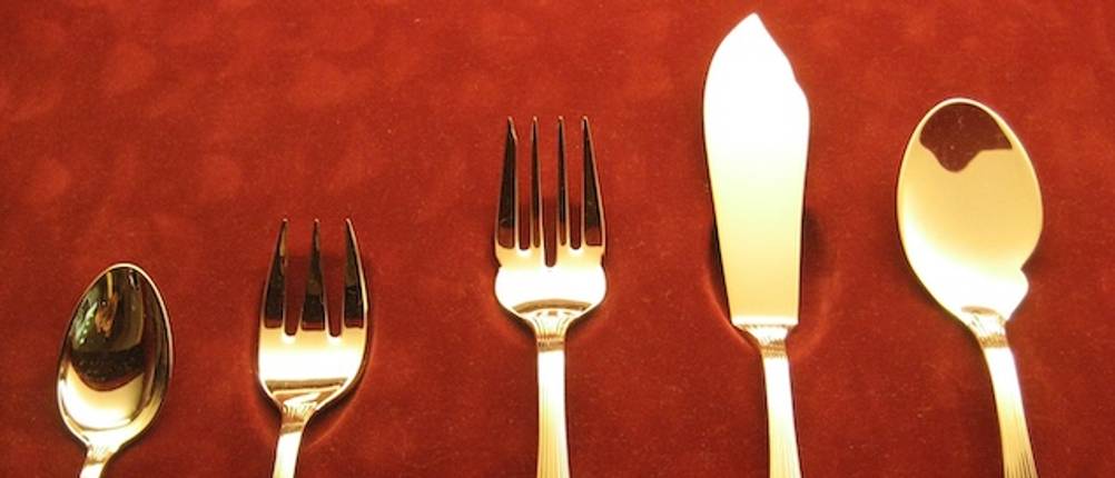 Besteck und Fischbesteck getestet: Nahaufnahme von einem vergoldetem Besteck-Set inklusive Fischbesteck auf rotem Untergrund.