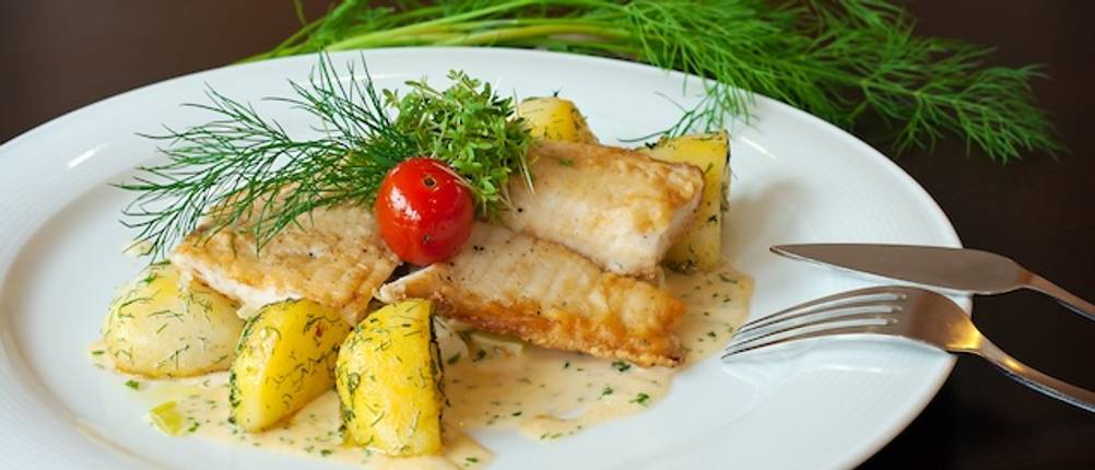 Fischbesteck mit einem Fischfilet neben Kartoffeln und Dill auf einem weißen Teller getestet.