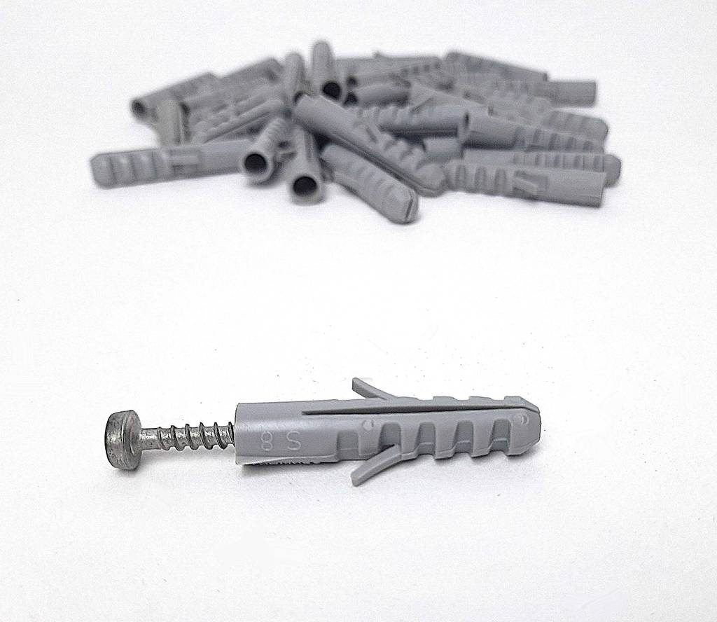 Vor einem Haufen grauer Dübel im Test liegt ein S-8-Dübel inklusive seiner Schraube.