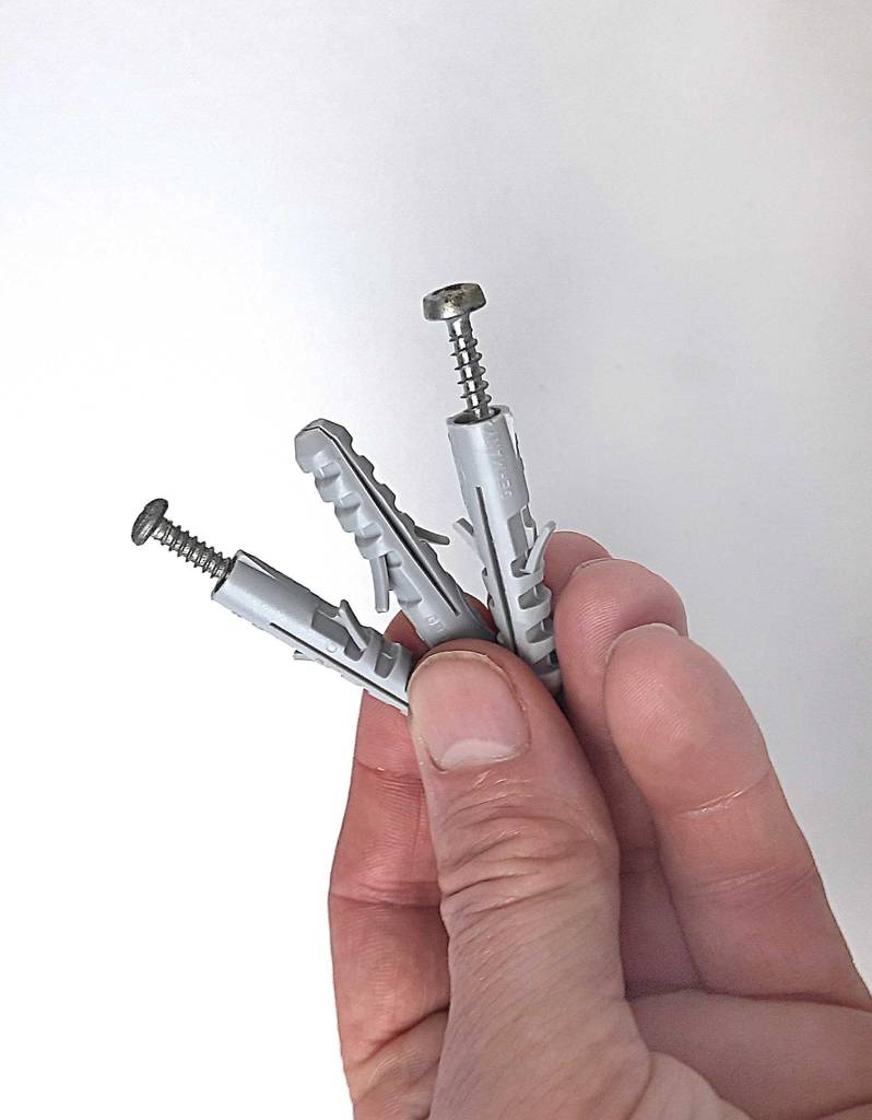 Eine Hand hält die getesteten Dübel inklusive Schrauben vor einer weißen Wand.