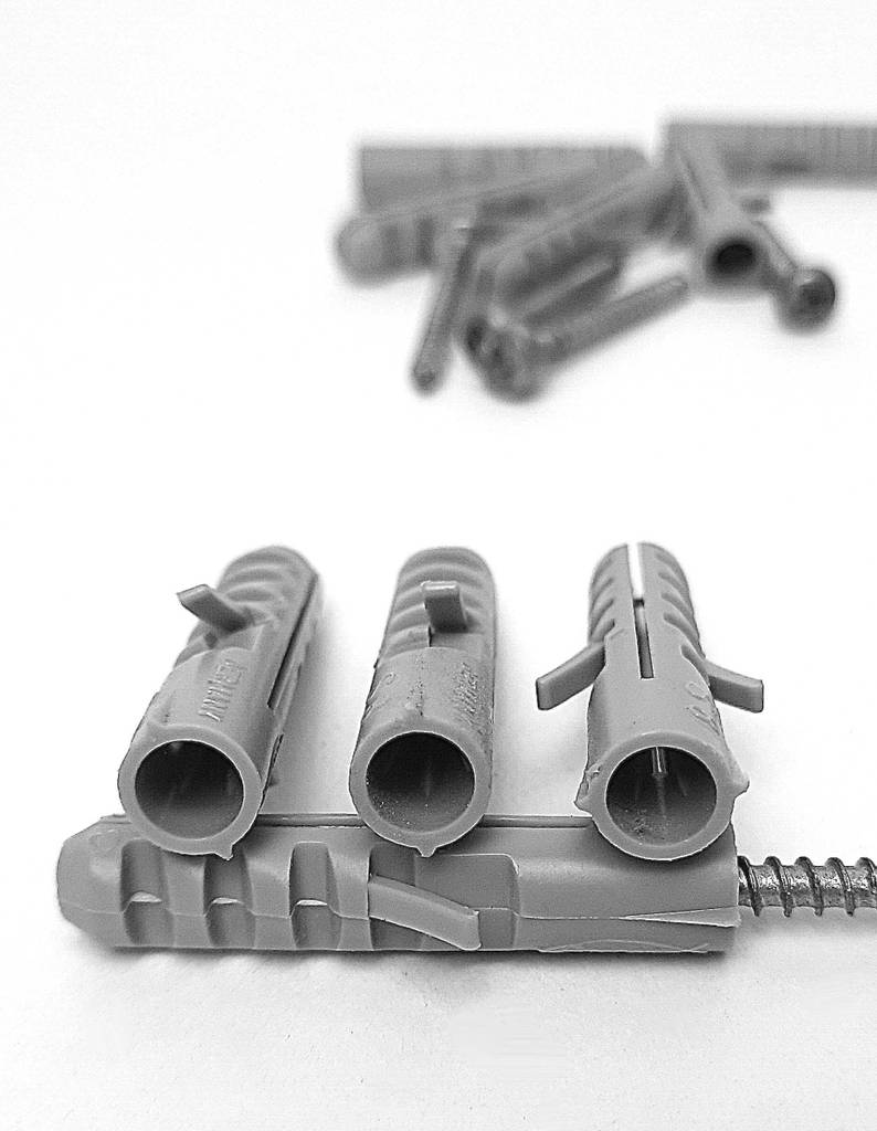 Im Test: Die Dübel in Hellgrau befinden sich übereinander, mit Fokus auf der Öffnung, auf einer weißen Oberfläche.