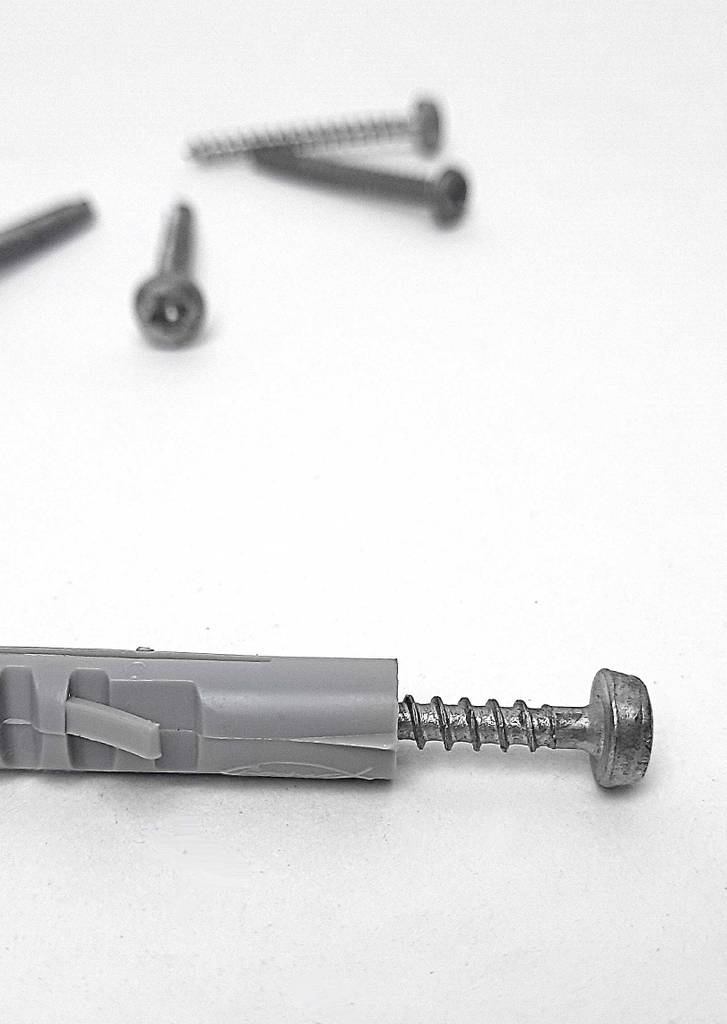 Ein grauer, getesteter Dübel liegt inklusive eingeschraubter Schraube vor mehreren Schrauben, die sich im Hintergrund befinden.