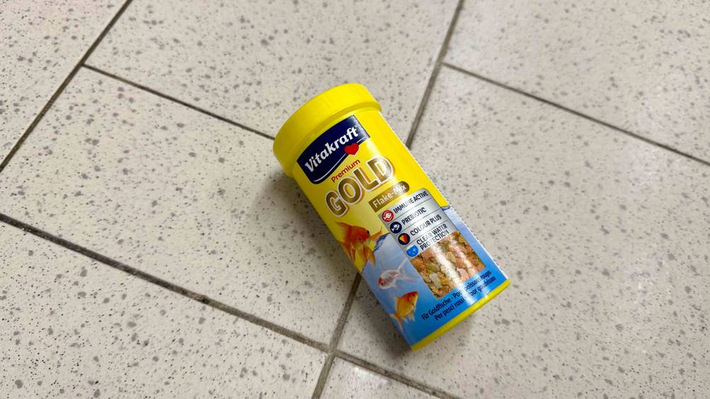 Auf einem Fließenboden liegt eine Dose des getesteten Fischfutters.