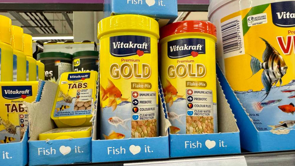 Mehrere Dosen des Fischfutters im Test in einem Verkaufsregal neben anderen Produkten.