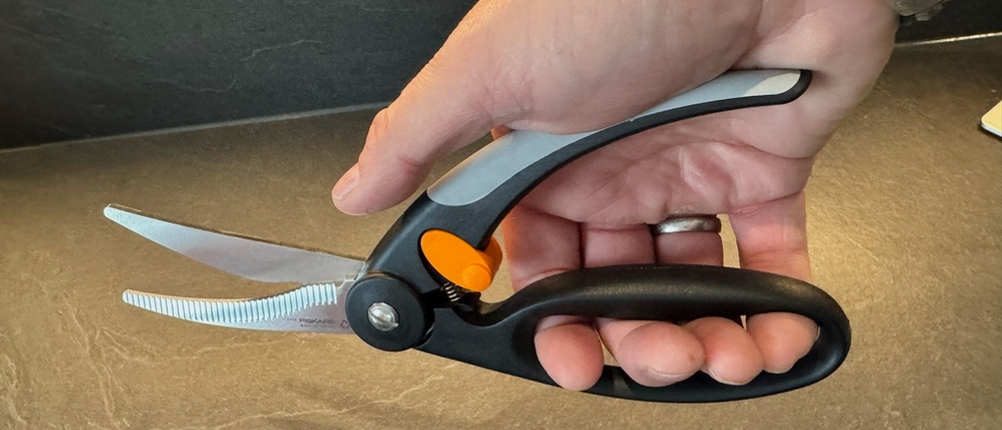 Eine Hand drückt die Fiskars 1003033 FF Geflügelschere zu