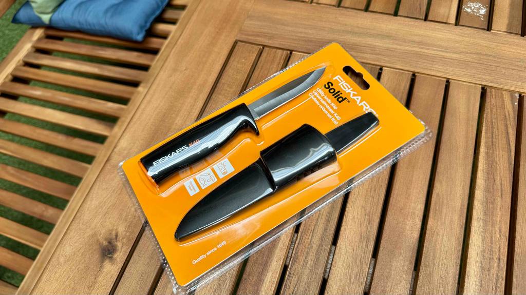 Ein Fiskars-Messer im transparenten Blister liegt zum testen auf einer Holzfläche.