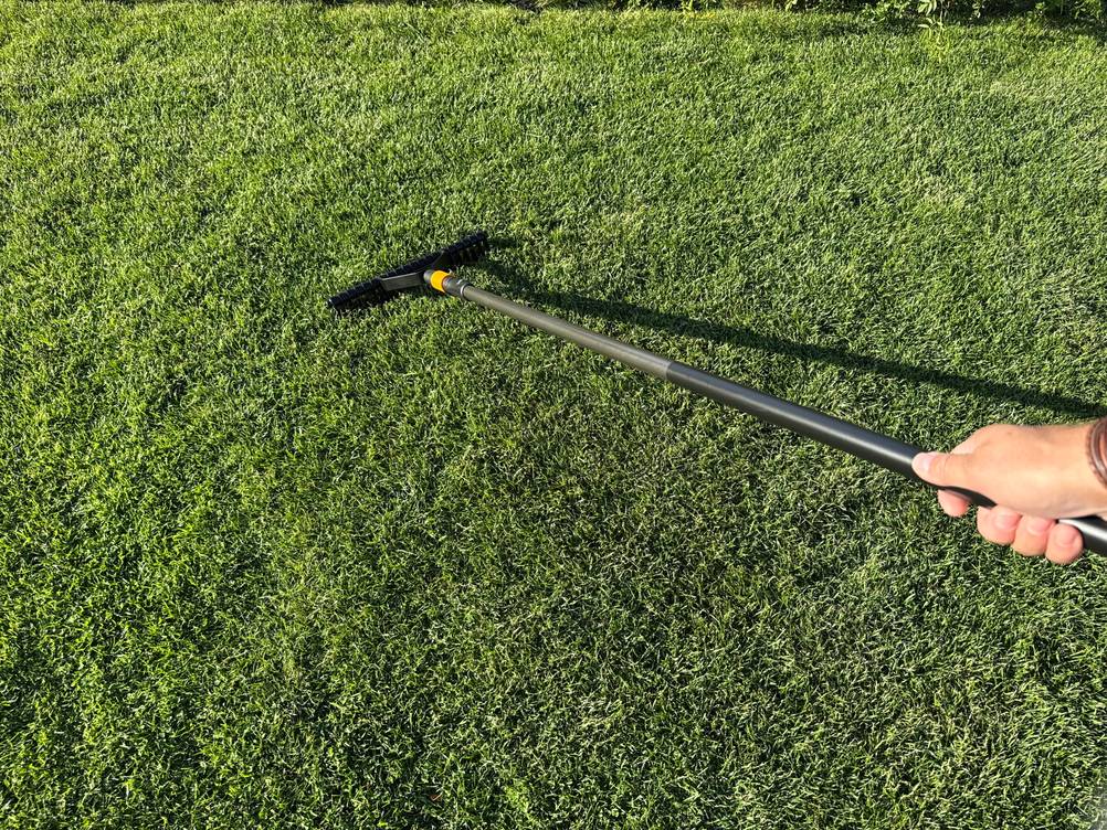 Eine Hand zieht den Fiskars-Rasenlüfter über eine Rasenfläche.