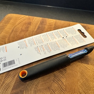 Der Sparschäler von Fiskars liegt auf einem hölzernen Küchenbrett.