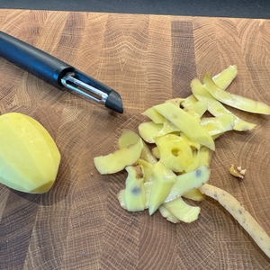 Der Fiskars Schäler neben einer geschälten Kartoffel und Kartoffelschalenstreifen.