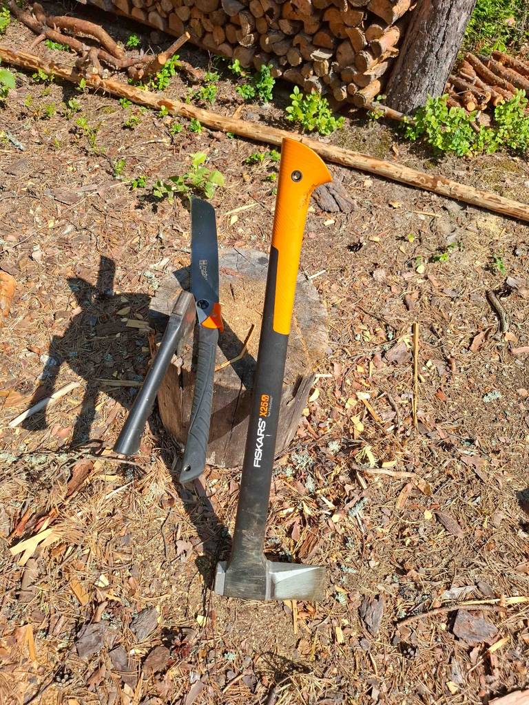 Die getestete Fiskars Axt lehnt neben einer Heckenschere an einem Holzstumpf.