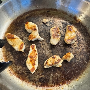 Stark angebratenes Hähnchen in der Fissler-Catania-Edelstahl-Pfanne und viele Bratenreste auf dem Boden