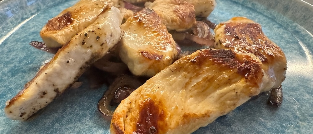 Hähnchenfleisch angebraten auf einem blauen Teller, darunter Zwiebeln