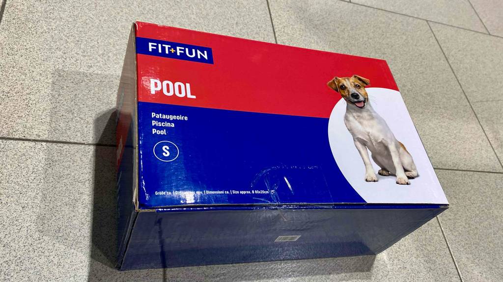 Eine blau-rote Verpackung mit einem getesteten Fit-Fun Hundepool der Größe S liegt auf einem Fliesenboden.