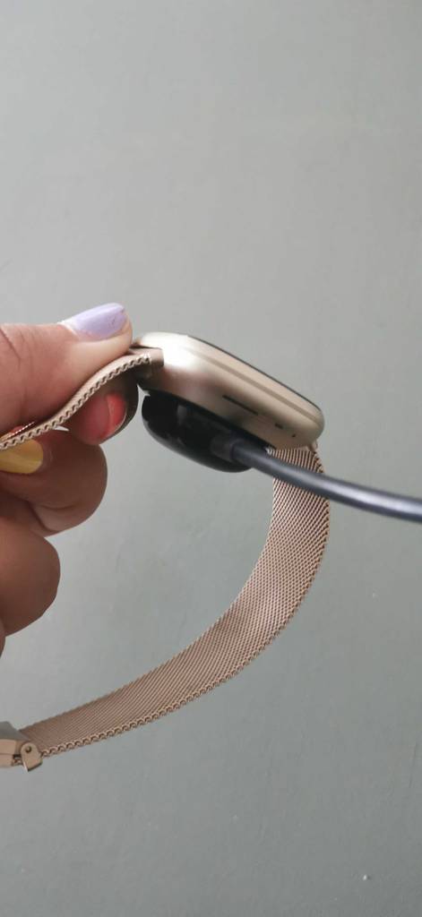 Ein getestetes Fitbit von der Seite an den Strom angeschlossen von einer Hand gehalten.