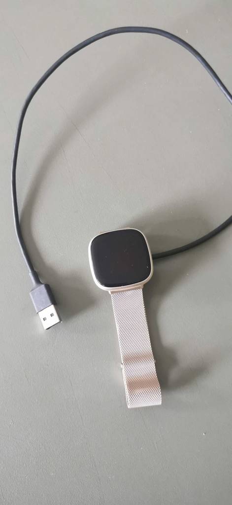 Getestete Fitbit mit eingestecktem USB-Kabel liegt auf weißer Fläche.