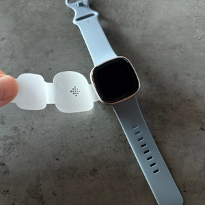 Eine Hand zieht einen Schutz von der Fitbit Versa 4 ab