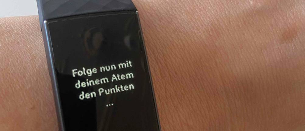 Fitness-Armband-Test: Nahaufnahme eines Fitness-Armbandes an einem Handgelenk mit einer Aufforderung zum bewussten Atmen