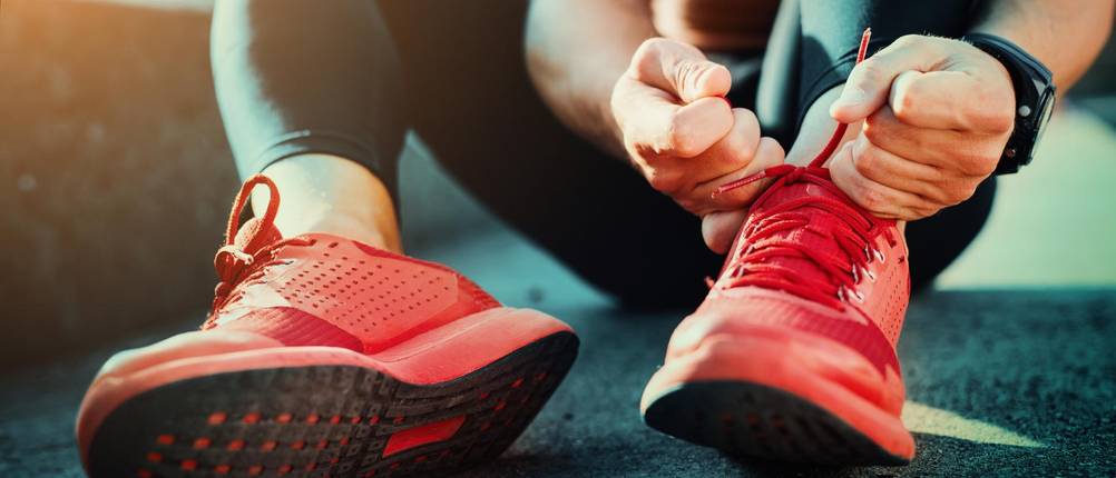 Fitnessschuh-Herren Test: Ein Mann zieht seine roten Fitnessschuhe an.