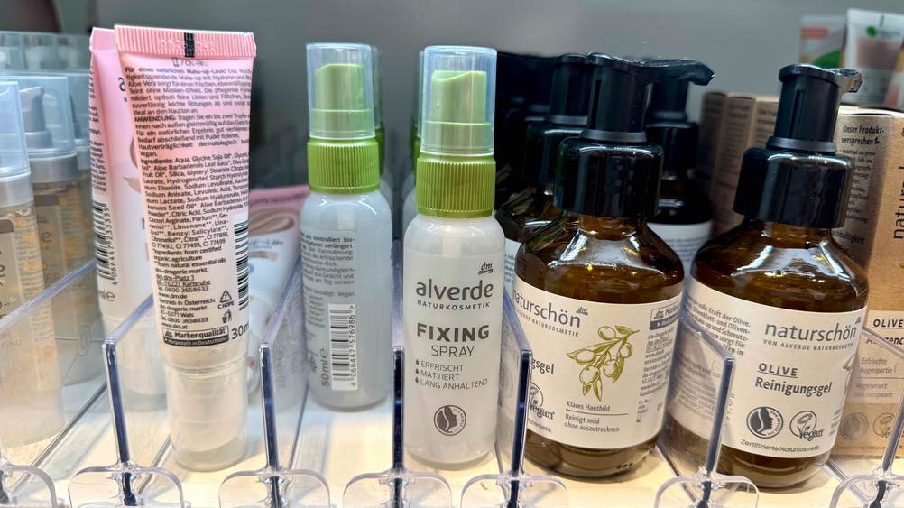Mehrere Flaschen des getesteten Fixing-Sprays stehen neben anderen Produkten in einem Verkaufsregal.
