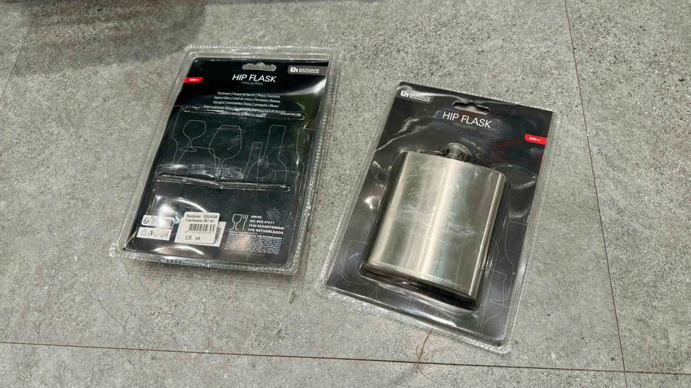 Getestet: Zwei verpackte Flachmänner, einer von vorne einer mit der Rückseite nach oben auf einem Fließenboden.