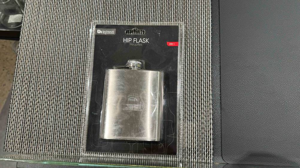 Ein getesteter Flachmann in seiner transparenten Verpackung auf einem grauen Stoff.