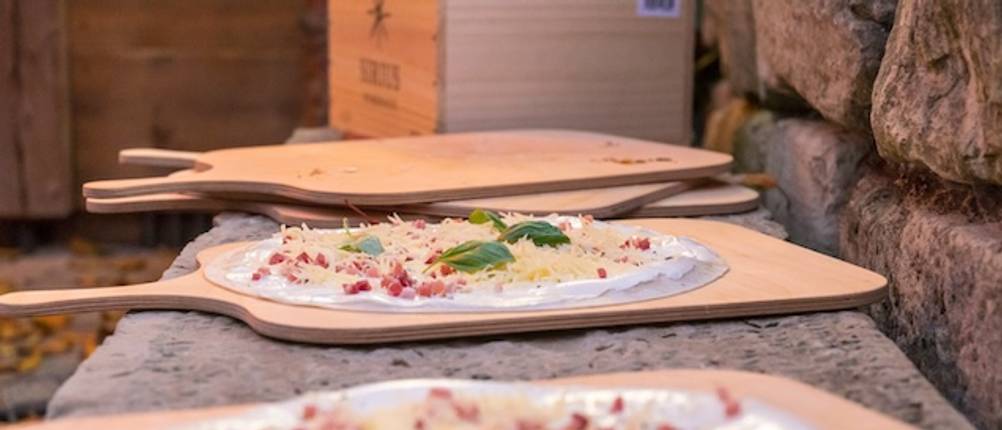 Flammkuchenbrett im Funktions-Test: Mehrere Flammkuchenbretter liegen auf einer rustikalen Ablagefläche, zwei davon sind mit einem noch ungebackenen Flammkuchen bestückt.