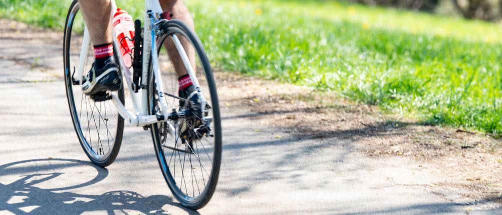 Rennrad-Flaschenhalter-Test: Ein Rennradfahrer fährt auf einer Straße davon; seine Trinkflasche ist im Halter am Rahmen angebracht.