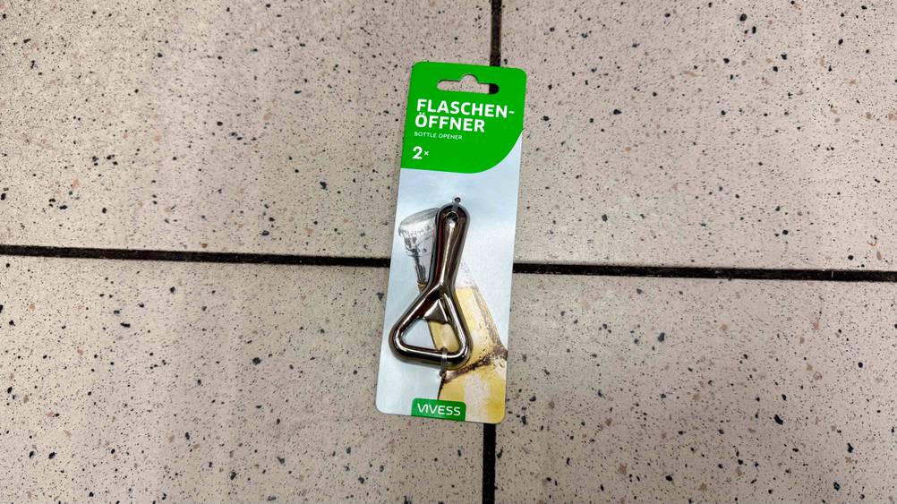 Auf einem. Fließeboden liegt ein verpackter Flaschenöffner im Test.