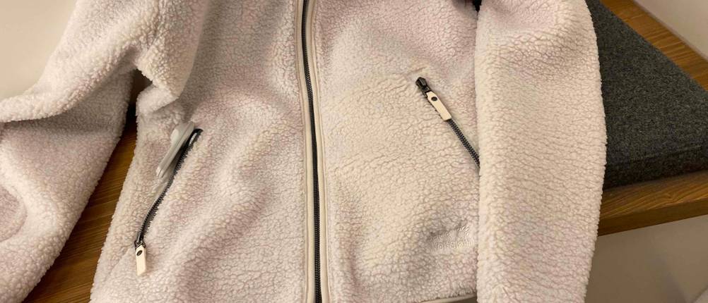 Nahaufnahme der geschlossenen Vorderseite einer getesteten Fleecejacke für Damen auf einer Holzbank.