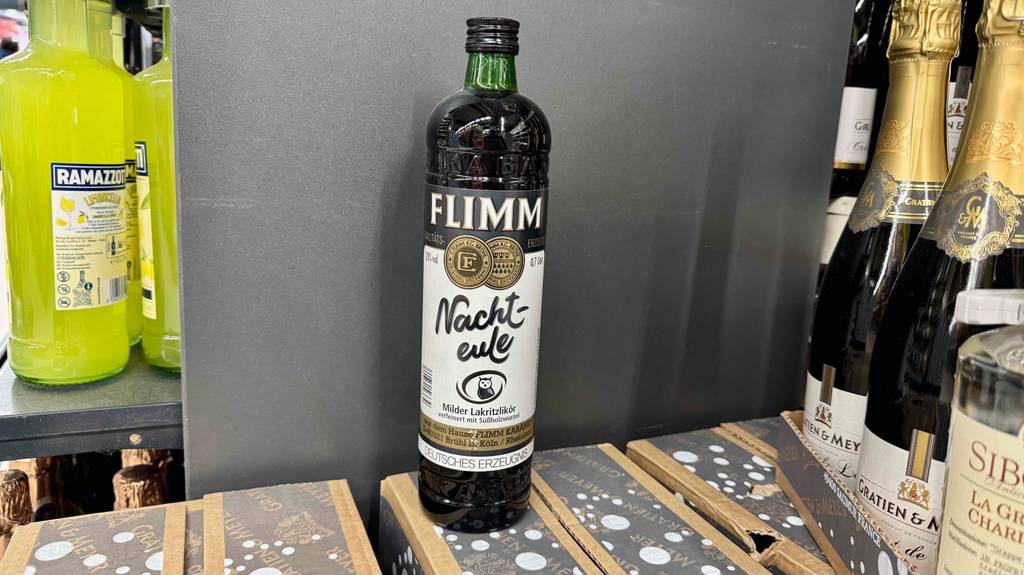 Eine grüne Flasche mit Lakritzlikör im Test steht auf einem Karton neben andere Likörflaschen.
