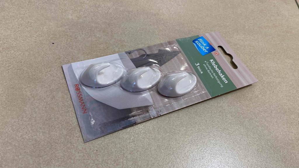 Klebehaken im Test: eine Verpackung von Flink-Sauber mit drei Klebehaken befindet sich auf einem hellen Untergrund.