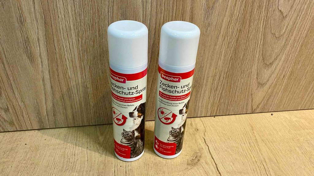Zwei Flaschen mit getestetem Flohspray für Katzen und Hunde befinden sich auf einem Holzregal. 
