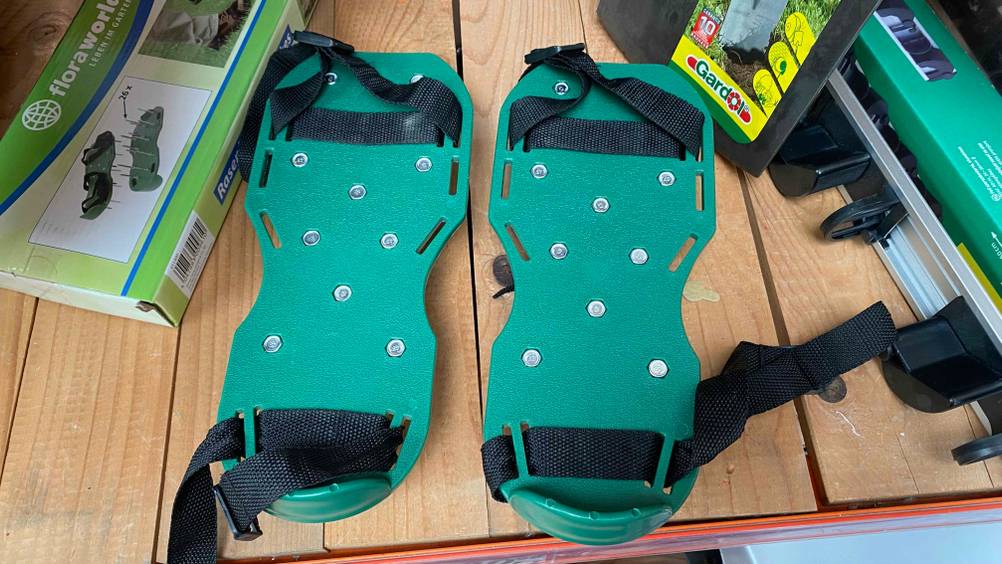 Ein Paar getestete Rasenlüfter-Schuhe nebeneinander zwischen anderen Produkten auf einem Holzregal.