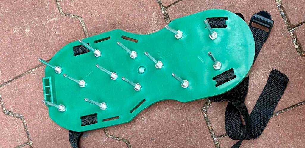 Getestete Rasenlüfter-Schuhe mit Gurten befinden sich auf einem roten Pflastersteinboden.