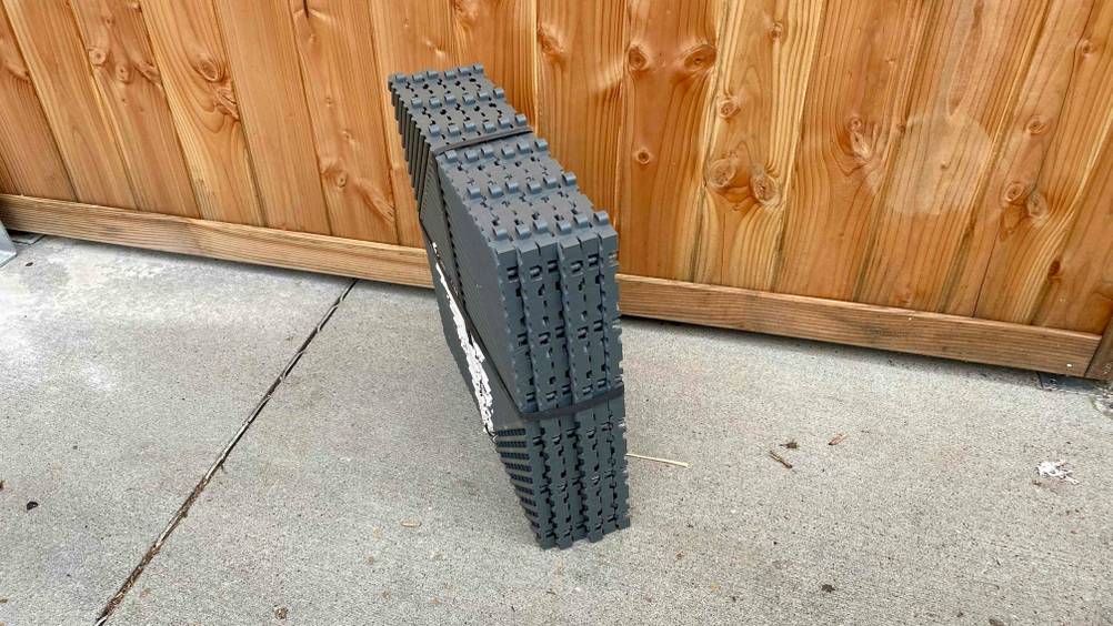 Terrassenplatte getestet: Ein Packet mit sechs Platten von der Seite vor einer Holzwand auf einem Betonboden stehend.