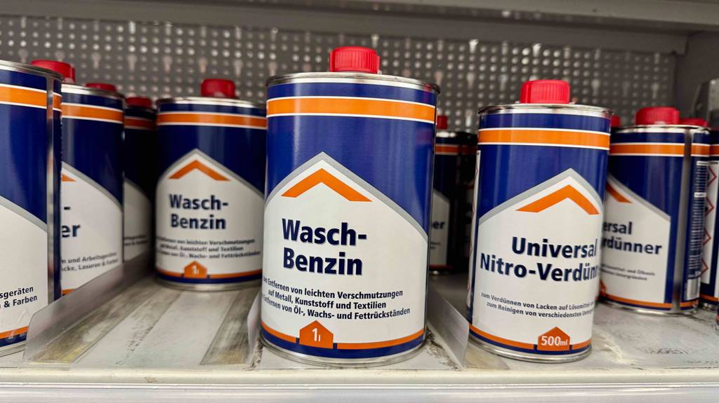 Waschbenzin im Test: Mehrere Dosen stehen zwischen anderen Produkten in einem Regal.